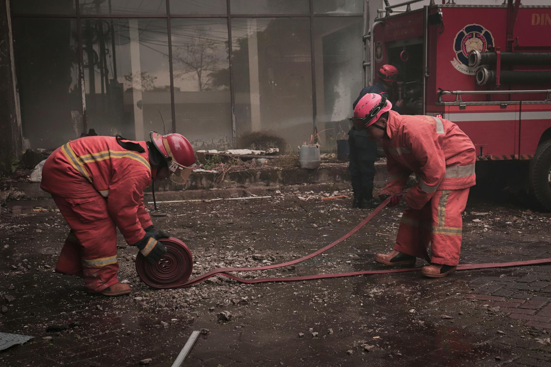 Strażacy rozwijają węże na mokrej jezdni w zabudowie miejskiej