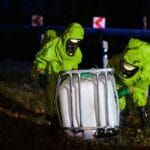Strażacy w kombinezonach chemicznych zabezpieczają wyciek na drodze nocą