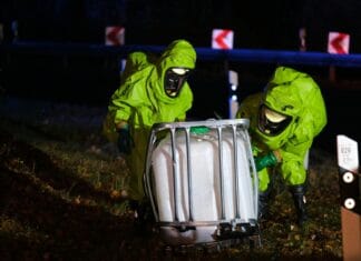 Strażacy w kombinezonach chemicznych zabezpieczają wyciek na drodze nocą