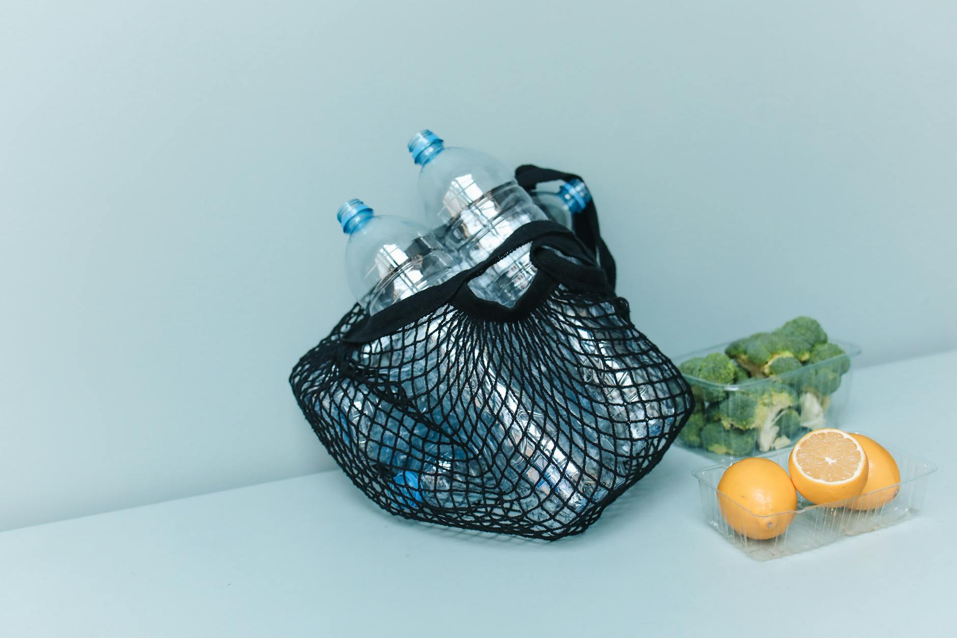 Siatka z plastikowymi butelkami, brokułem i cytrynami jako symbol zero waste