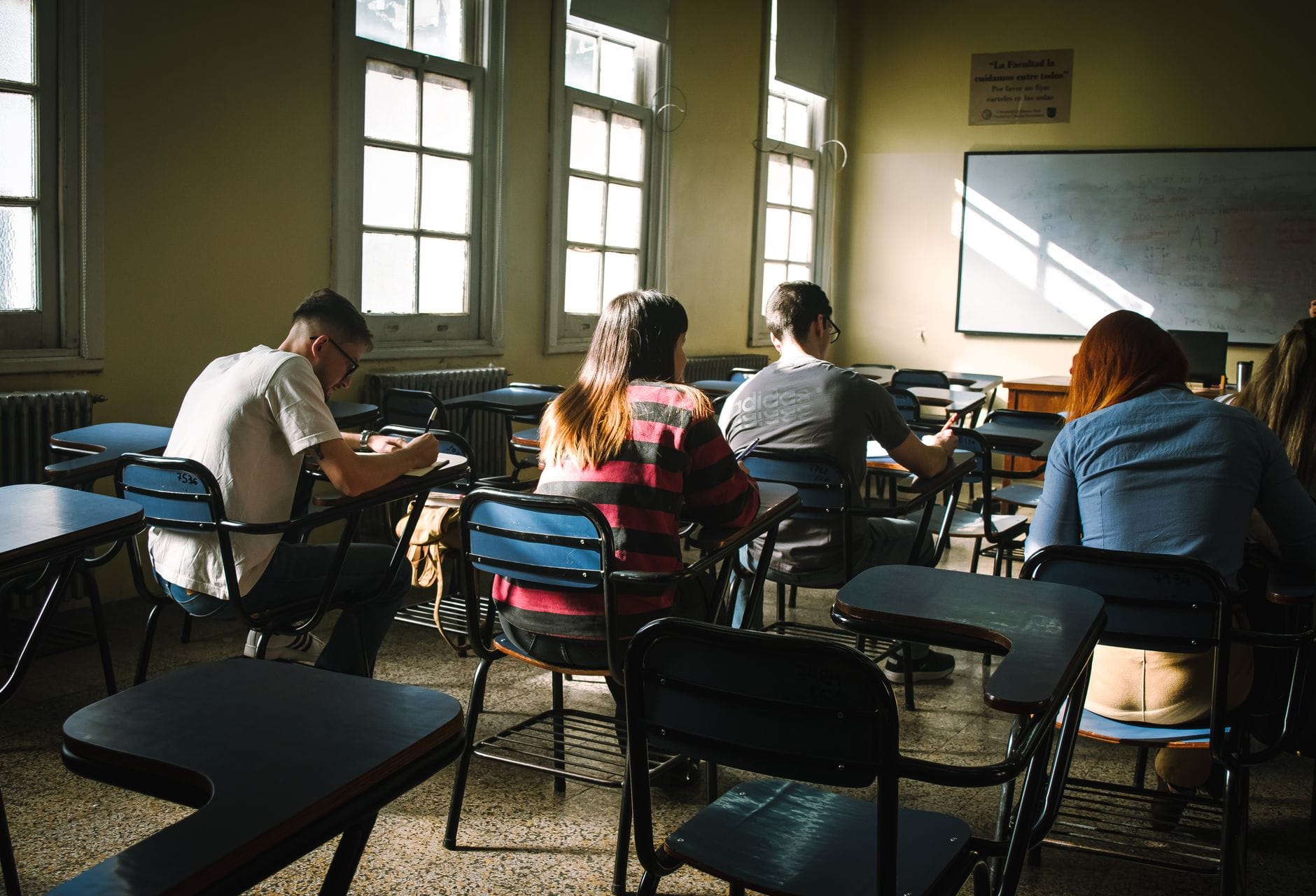 Studenci rozwiązują test w jasnej sali egzaminacyjnej